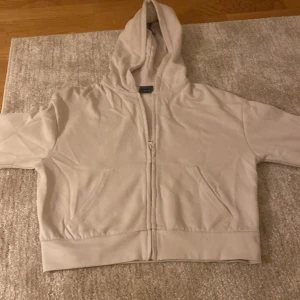 Beige hoodie med dragkedja - Beige hoodie med huva och hel dragkedja framtill. Tröjan har två fickor på framsidan och är tillverkad i mjukt bomullsmaterial. Passformen är normal och modellen är klassisk med långa ärmar. Perfekt för chill dagar och enkel att matcha.