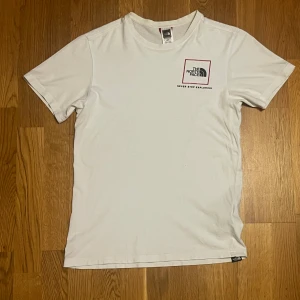 The NorthFace Tshirt - Snygg och stilren vit t-shirt från The North Face med logga och texten “Never Stop Exploring” på bröstet. Storlek XS herr. Fint skick,med ett par små, nästan osynliga hål på framsidan – därav priset.