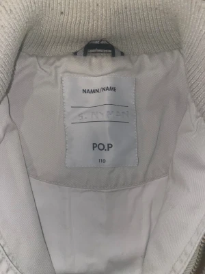 Ljusgrå barn jacka från Polarn O. Pyret - Snygg ljusgrå barn jacka från Polarn O. Pyret med ribbad krage och muddar. Jackan har två framfickor med knappar och dragkedja framtill. Perfekt för dig som gillar stilren och enkel design med coola detaljer.