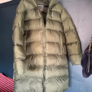 Olivgrön lång dunjacka Haglöfs XL - Säljer en olivgrön lång dunjacka från Haglöfs i storlek XL . Jackan har huva, quiltad design och dragkedja framtill. Perfekt för kalla dagar och har en clean, modern look som funkar till streetstyle. Materialet är syntet och dun. Den sista bilden ger rätt färgnyans, svårt att fota o få rätt i annat ljus,  Den är helt ny och säljs pga att den blivit för stor för mig. Superfin!