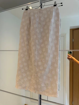 Beige omlottkjol med knut från H&M - Snygg vit långkjol från H&M med subtilt prickmönster, omlottmodell och knutdetalj i midjan. Materialet är en mix av viskos, polyamid och polyester, vilket gör den lätt och skön att bära. Crémevit midikjol med mönstrat prickigt tyg, draperad dekorativ knut och slits framtill. Perfekt till julfest, nyår, osv.