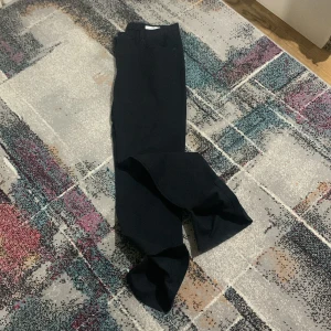 Svarta kostymbyxor från Bläck - Snygga svarta kostymbyxor från Bläck med klassisk rak passform och diskreta slitsar vid bensluten. Byxorna har midwaist och är tillverkade i ett mjukt bomullsmaterial som ger en stilren look. Perfekta för dig som gillar minimalistisk stil.