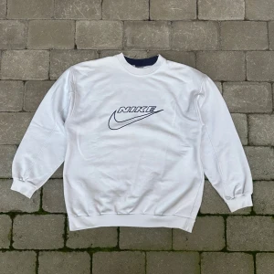 Vintage 90s Nike vit sweatshirt / crewneck  - Vit vintage sweatshirt med en broderad Nike-logga framtill och en mörkblå kant runt halsen. En äkta retro klassiker från Nike med den sköna street stilen. Tröjan är i mycket bra skick. Det som finns att anmärka är en fläck på vänster arm (se sista bilden) denna går med största sannolikhet bort i tvätten.  ﻿ ﻿mått  ﻿längd: 75cm  ﻿armhåla till armhåla: 60cm 
