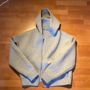 Grå scuba hoodie från Weekday med dragkedja - Säljer en stilren grå scuba hoodie från Weekday i storlek M. Tröjan har huva, hel dragkedja framtill och två fickor. Materialet är mjuk bomullsmix som känns skön mot huden. Perfekt för chill dagar eller när du vill ha en enkel look.