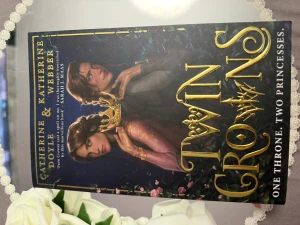 Twin Crowns - En magisk och spännande bok om två prinsessor och en tron, perfekt för dig som gillar fantasy, intriger och starka karaktärer. Omslaget är färgstarkt med gulddetaljer och ger en episk känsla. Passar unga vuxna som vill försvinna in i en annan värld.