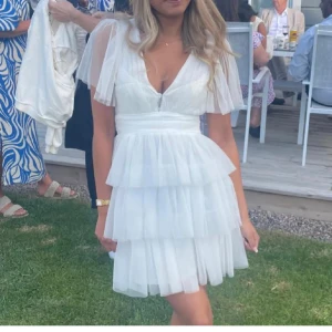 Studentklänning - Superfin vit kortklänning med flera lager volanger och v-ringad omlott överdel. Klänningen har transparenta, korta ärmar och markerad midja. Perfekt för dig ska ta studenten! Klänningen står att den är i storlek M men jag har alltid S och den passar perfekt på mig så någon som har stolek M hade den nog varit för liten för.🥰