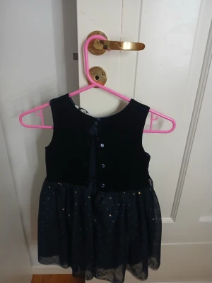 Mörkblå sammetklänning med glitter - Supersöt mörkblå klänning från Cubus i sammet med ärmlös överdel och knappar bak. Kjolen är i tunn tyll med små glittriga prickar och en dekorativ blomma i midjan. Perfekt för dig som vill sticka ut med lite extra glitter och mjuk sammet.