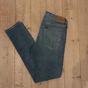 Blå jeans från Lee - Snygga blå jeans från Lee med klassisk femficksdesign och brunt Lee-läderpatch bak. Slim fit