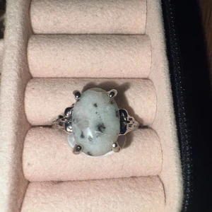 Silverring med oval ljus sten, storlek 20 - Snygg silverfärgad ring med en stor oval ljus sten som har naturliga mörka inslag. Ringen har detaljerade klor som håller stenen på plats och en klassisk, elegant design. Perfekt för dig som gillar unika smycken med lite vintagekänsla.