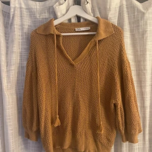 Stickad brun tröja från Zara - Säljer en stickad brun tröja från Zara med snygg krage och v-ringning. Tröjan har trekvartslånga ärmar, ribbade muddar och snörning med tofsar.🧡