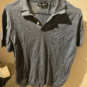 Blå kortärmad skjorta från Zara - Blå skjorta från Zara med klassisk krage och två knappar framtill. Skjortan är kortärmad och har en enkel, stilren design i mjukt bomullsmaterial. Perfekt för dig som gillar en chill och avslappnad look.