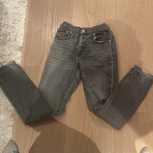 Grå skinny jeans från Levi's - Snygga grå jeans från Levi's med klassisk femficksdesign och smal passform. Jeansen har en mörkgrå tvätt med subtila slitningar och silverfärgade nitar. Perfekt för dig som gillar en stilren och modern look.