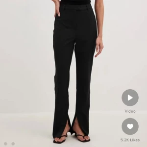 Svarta kostymbyxor med slits - Snygga svarta kostymbyxor med hög midja och raka ben. Byxorna har en cool slits framtill vid bensluten som ger en trendig touch. Passar perfekt till sneakers eller klackar. Klassisk look med bälteshällor och diskreta fickor bak.