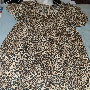Leopardmönstrad klänning från Monki - Säljer en snygg leopardmönstrad klänning från Monki i storlek M. Klänningen har korta puffärmar och en luftig passform. Färgerna går i beige, svart och brunt. Perfekt för dig som vill sticka ut med ett djurmönster. Materialet känns lätt och bekvämt.