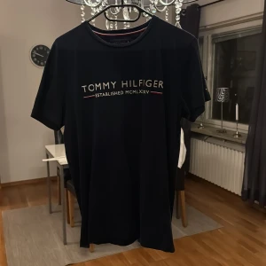 Svart Tommy Hilfiger t-shirt S - Svart t-shirt från Tommy Hilfiger i ekologisk bomull. Klassisk rund hals med röd och vit rand på insidan, tryckt logga framtill och liten Hilfiger-flagga på ärmen. Snygg och stilren modell med korta ärmar, perfekt för dig som gillar ikoniska märken.