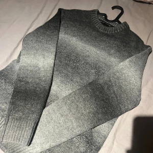 Grå stickad tröja med rund hals - Snygg stickad tröja! Tröjan har rund hals, ribbade muddar och långärmad passform. Perfekt för dig som gillar stilrena och enkla plagg med lite edge. Passar dig som vill ha en chill och bekväm look.