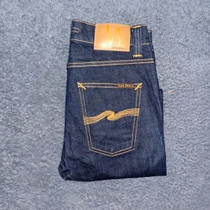 Nudie Jeans  - Mörkblå Lean Dean jeans från Nudie Jeans i storlek 28/32. Modellen har smal passform och klassisk femficksdesign med orangea sömmar och Nudie-logga på bakfickan. Midja 34cm, längd 104cm.  Ifall det inte finns någon bild i annonsen där jag bär plaggen jag säljer så är det för att jag ej kan ha storleken heller passformen, så kolla måtten för storlek och googla på modellnamnet för passform 😉43