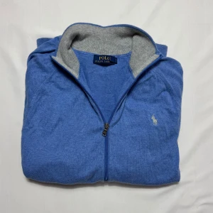 Full zip tröja Ralph Lauren  - Blå kofta från Polo Ralph Lauren i storlek XL men passar mer som M-L med grått ribbstickat foder i kragen. Tröjan har dragkedja framtill och den klassiska broderade loggan på bröstet. Perfekt för dig som gillar stilren design och vill ha något bekvämt och snyggt.                                                         Tveka inte att höra av dig vid minsta fundering!