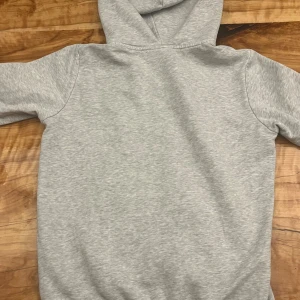 Grå hoodie från Peak Performance - Snygg ljusgrå hoodie från Peak Performance med hel dragkedja och broderad logga på bröstet. Tröjan har huva, två fickor fram och är tillverkad i mjuk bomullsmix med fleece på insidan. Perfekt för chill eller träning, passar dig som gillar enkel och clean stil.