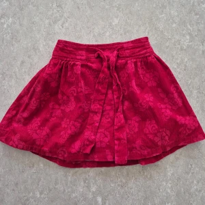 Kjol - Supersöt röd kortkjol från FIX i manchester med blommigt mönster. Kjolen har knytband i midjan och volangig tyllkant på insidan för extra fluff. Perfekt för dig som gillar färg och detaljer!