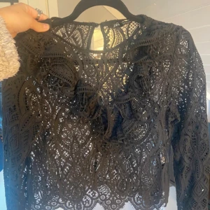 Svart spetsblus från Zara - Säljer en svart blus från Zara med långärmad design och detaljerad spets. Blusen har vackra broderade mönster och volang framtill, vilket ger en cool och elegant vibe. Perfekt för dig som gillar unika plagg med mycket detaljer. Använt bara 2 gånger. Skriv för mer bilder!💗