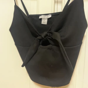 Svart croppad linnetopp från Amisu - Snygg svart croppad linnetopp från Amisu med smala axelband och knytning framtill. Toppen har en enkel och stilren design som passar perfekt till jeans eller kjol. Tillverkad i polyester för en mjuk och följsam känsla.