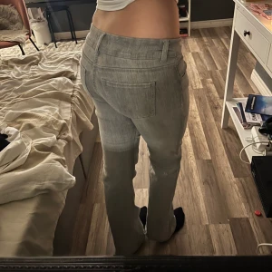 Grå bootcut jeans med låg midja - Snygga grå jeans med bootcut passform och låg midja. Klassisk femficksmodell med bälteshällor och raka ben. Perfekta för dig som gillar en avslappnad och trendig stil. Materialet är jeans och färgen är ljusgrå.