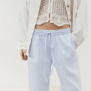 Ljusblå randiga linnebyxor med snörning - Snygga ljusblå linnebyxor med tunna vita ränder och avslappnad passform. Byxorna har elastisk midja med snörning och utsvängda ben, perfekta för en chill och fräsch look. Luftigt material som passar när du vill vara bekväm. Byxorna är för små därför säljes, använda 2 gånger. Skriv för fler bilder🥰