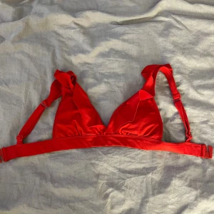 Röd bikiniöverdel med volang från KappAhl - Snygg röd bikiniöverdel från KappAhl i storlek XS. Modellen har volangdetaljer vid kuporna och justerbara axelband för perfekt passform. 