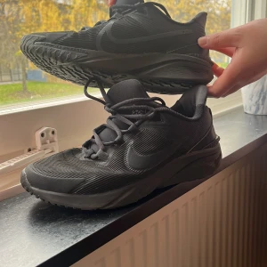 Svarta Nike sneakers strl 40 - Säljer ett par helsvarta Nike sneakers med snygg, sportig design och diskret swoosh på sidan. Skorna har snörning, slitstark sula och är tillverkade i syntetmaterial. Perfekta för dig som gillar en clean och stilren look.