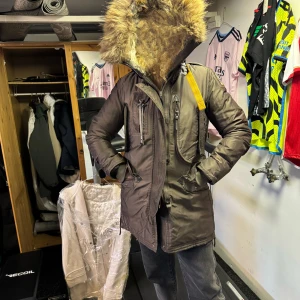 Brun Parajumpers parkajacka med päls - Säljer en brun Parajumpers parkajacka med stor fluffig päls på huvan, cool gul detaljrem och patch på ärmen. Jackan har flera fickor, quiltad insida och dragkedja framtill. Perfekt för dig som vill ha en varm och snygg jacka med streetvibe. Varm och skön, liten lagning av innertyget inne i en ärm, ej synligt när på (se foto). Rymlig, storlek XS, jag är M och den sitter skönt.