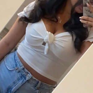 Vit croppad topp med knyt från SHEIN - Supersöt croppad topp från SHEIN i ljusvit färg med ribbad struktur. Toppen har offshoulder och korta puffärmar med resår, samt en stor knytning framtill som ger en extra stylish vibe. Perfekt till jeans eller kjol för en chill look.