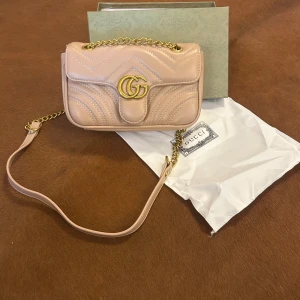 Beige quiltad axelväska från Gucci - Supersnygg beige axelväska från Gucci i mjukt skinn med quiltad design och guldfärgade detaljer. Väskan har kedjerem och klassiskt GG-spänne framtill. Perfekt storlek för det viktigaste och en riktigt lyxig vibe.