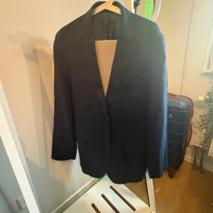 Mörkblå kavaj Dressmann linne slim - Snygg mörkblå kavaj från Dressmann i ren linne, slim fit-modell. Klassisk design med två fickor framtill, smala slag och fyra knappar vid ärmslutet. Perfekt för dig som gillar stilrena och moderna plagg.