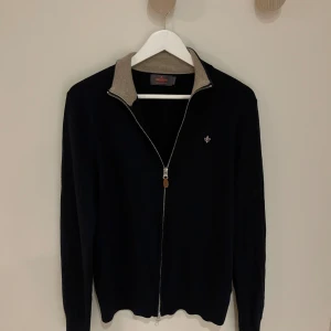 Marinblå tröja från Morris - Marinblå tröja från Morris i 100% merinoull med beige krage. Tröjan har hel dragkedja framtill och långärmade ärmar. Perfekt för dig som gillar stilrena och klassiska plagg med snygga detaljer. Tröjan är i XS-S men det står M (krympt). Priset går att diskutera…