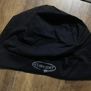 Svart mössa från Starlight LIMITED edition (one size) - Svart mössa från Starlight med broderad logga framtill i grått. Tillverkad i mjuk bomull, perfekt för kyliga dagar. Enkel och stilren design som passar till det mesta.