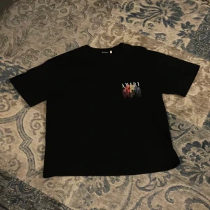 Svar  t-shirt med färgglatt tryck - Svart t-shirt  med coolt färgglatt tryck på bröstet och ryggen. Trycket har en drip-effekt i rött, orange, gult, grönt, blått och lila. Klassisk passform med rund hals och korta ärmar. Perfekt för dig som vill sticka ut med streetstyle.