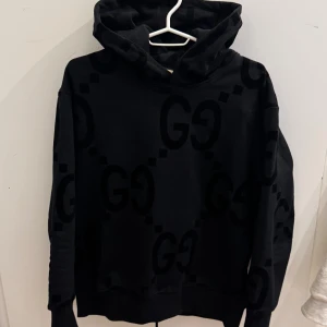GUCCI HOODIE - Svart hoodie från Gucci med stora GG-loggor i sammet över hela tröjan. Tröjan har huva, långa ärmar och ribbade muddar vid ärmslut och nederkant. Snygg och lyxig streetwear med en oversized passform som sticker ut. 