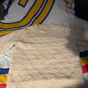 Beige stickad tröja från Zara Man - Säljer en beige stickad tröja från Zara Man med snyggt strukturerat mönster över hela tröjan. Den har rund hals och långa ärmar, perfekt för att hålla sig varm och ändå se fräsch ut. Passar dig som gillar stilrena och neutrala färger.