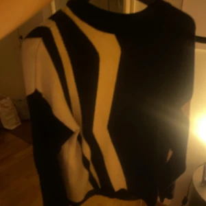 Stickad tröja - Säljer en stickad tröja med coolt grafiskt mönster i svart och beige. Tröjan har långärmade och en rund halsringning. Passar dig som gillar att sticka ut med snygga kontraster och unika detaljer i din outfit.