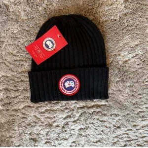 Svart ribbad mössa från Canada Goose - Svart ribbstickad mössa från Canada Goose med klassisk rund logotyp-patch framtill i rött, vitt och blått. Snygg uppvikt kant och mjukt material som håller dig varm. Perfekt för kalla dagar och har en clean, stilren look som funkar till allt. Äkta fick i present men tycker det är för flashy och skriker rik
