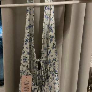 Blommig halterneck topp från Nelly - Supersöt halterneck topp från Nelly som är är öppen i ryggen och är vit med blåa blommönster. Toppen har knytning fram och volangkant nedtill, st xs och är helt ny och även då helt oanvänd. Kan ta fler bilder vid efterfrågan🩵🩵
