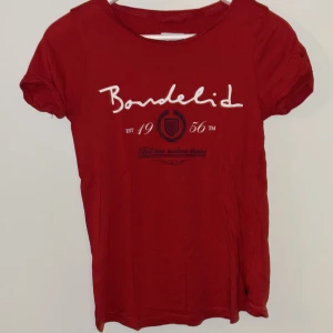 Röd t-shirt från Bondelid XS - Snygg röd t-shirt från Bondelid i storlek XS med tryck på bröstet och rund hals. T-shirten har korta ärmar och är gjord i mjuk bomull, perfekt för dig som gillar klassisk stil med en modern touch.