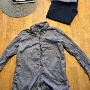 Grå oxfordskjorta från GANT - Snygg grå oxfordskjorta från GANT med klassisk button-down krage och vita knappar. Skjortan har lång ärm och ett litet broderat GANT-logo på bröstet. Perfekt för dig som gillar stilrena och tidlösa plagg. Materialet är mjuk bomull.