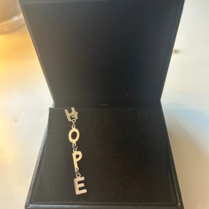 Silverfärgat HOPE örhänge - Unikt örhänge i silverfärg med hängande bokstäver som bildar ordet HOPE. Bokstäverna är fästa på en kedja som ger ett coolt och personligt uttryck. Perfekt för dig som vill ha ett statement-smycke med budskap.