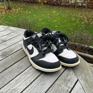 Nike Dunk Low svart/vit sneakers - Säljer ett par klassiska Nike Dunk Low sneakers i svart och vitt. Skorna har svart swoosh, svart snörning och perforerad tåbox för extra ventilation. Ovandelen är i skinn och de har en platt sula. Perfekt för dig som gillar streetstyle och tidlös design. Är ett litet hål i båda hälarna men varken känns eller syns när man har på de, jättefina i skinnet. Skriv vid minsta fundering eller fråga/bild. 