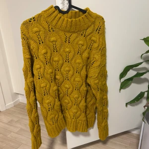 Gul stickad polotröja med mönster - Säljer en snygg gul stickad polotröja med unikt hålmönster och bred ribbad krage. Tröjan har långärmade ärmar och grovstickad struktur som ger en cool och trendig vibe. Perfekt för dig som gillar färg och vill sticka ut.