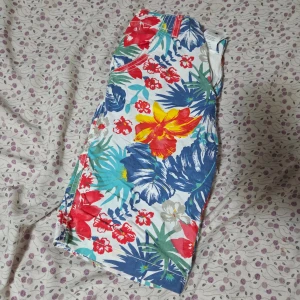 Färgglada blommiga shorts Knot So Bad - Säljer ett par sjukt färgglada shorts från Knot So Bad i storlek XS 14. De har ett blommigt mönster med röda, gula, blå och gröna toner på vit botten. Modellen är midwaist med fickor och dragkedja framtill. Perfekta för sommarens alla äventyr!