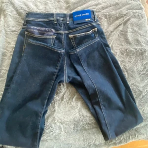 Jacob Cohën mörkblå jeans Bard LTD Ny pris 8000kr - Snygga mörkblå jeans från Jacob Cohën, modell Bard LTD. Klassisk femficksdesign med kontrastsömmar och blå patch bak . Kommer med en prickig näsduk i bakfickan och exklusiv orange tag. Perfekt för dig som gillar premiumjeans med stil.