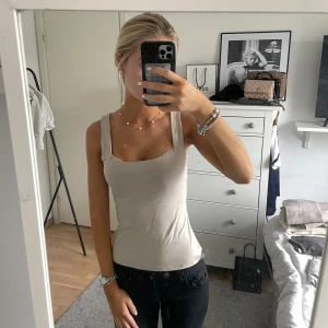 Beige linnetopp med breda axelband - Säljer en stilren beige linnetopp med breda axelband och fyrkantig ringning. Toppen är figurnära och har en enkel, clean look som passar perfekt till jeans eller kjol. Materialet känns mjukt och stretchigt, troligtvis bomull eller en bomullsblandning.